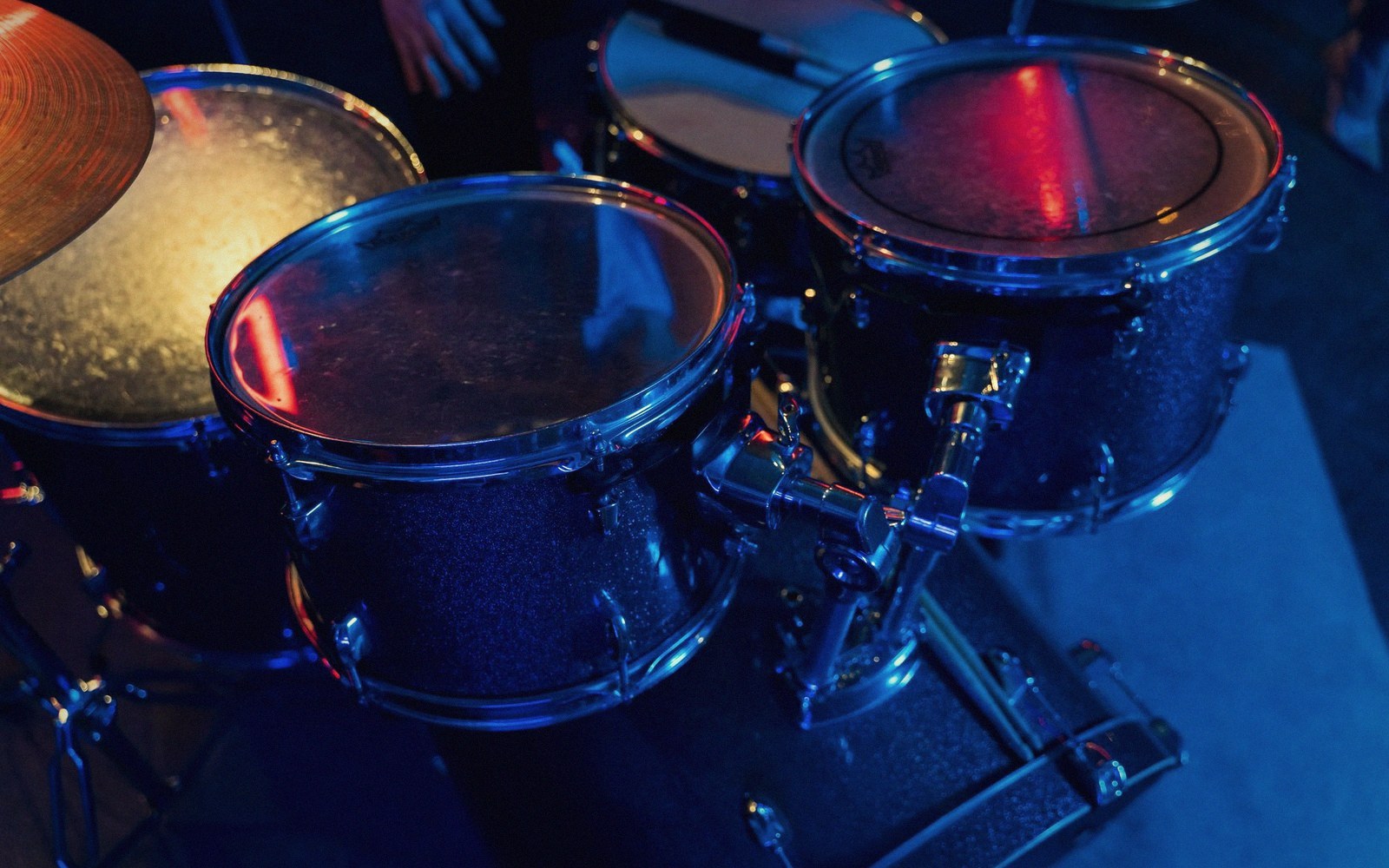 Close-up of drum kit toms and cymbal bathed in blue and red stage lighting