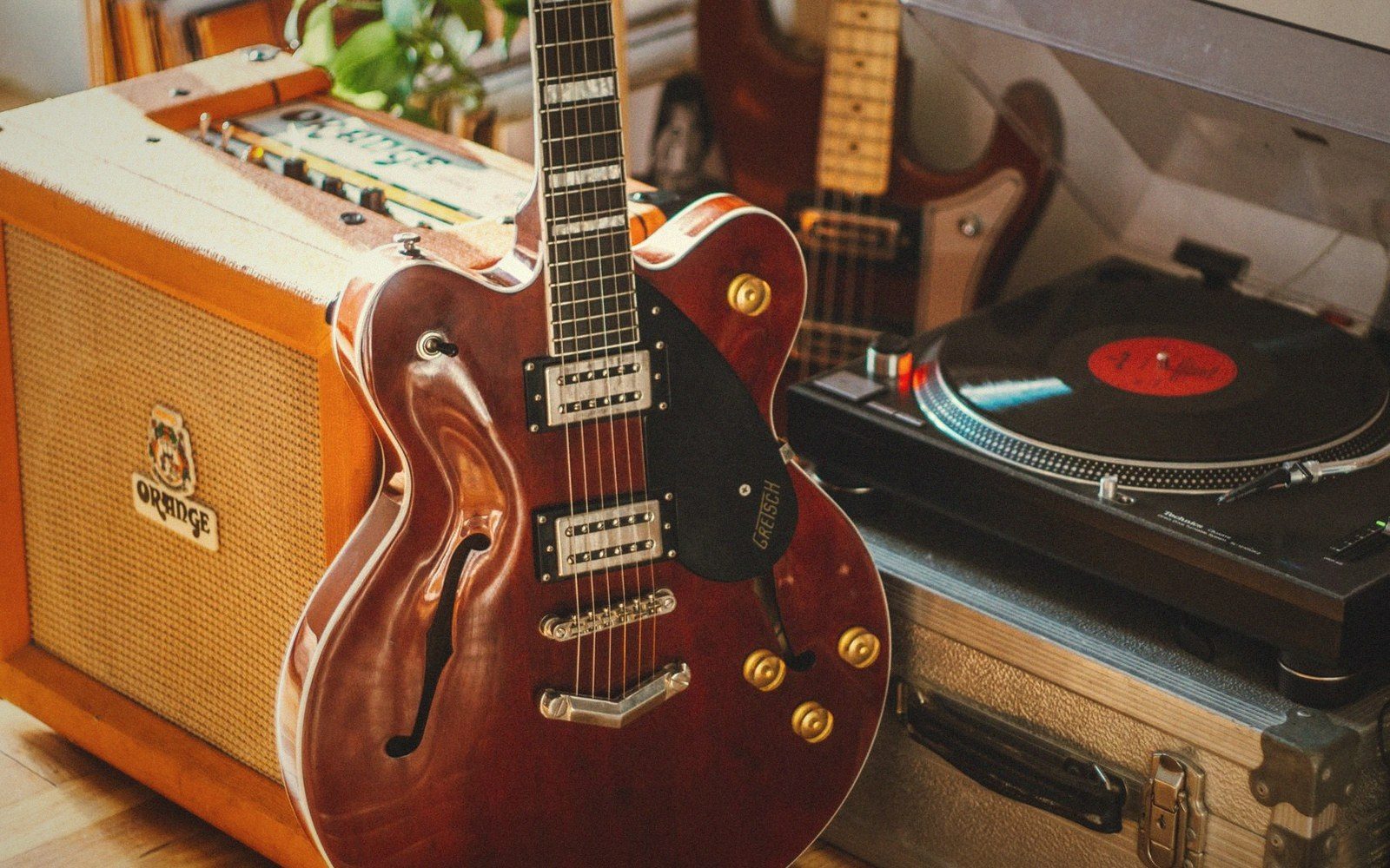 A hollow-body electric guitar leans against an amp beside a spinning turntable