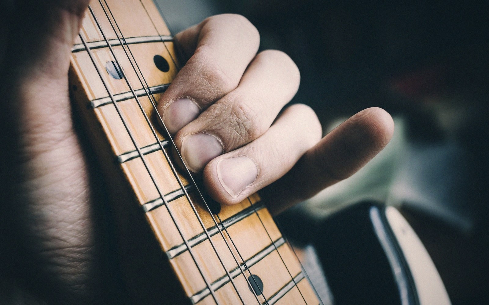 Close-up of fingers pressing down strings on a guitar's maple fretboard